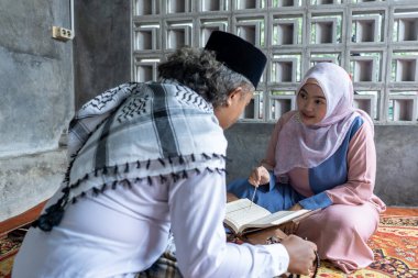 Kur 'an okumayı öğreniyorlardı. İki Endonezyalı kadın ve erkek evde Kur 'an okumayı öğreniyor. Kuran 'ı okuyorlar.
