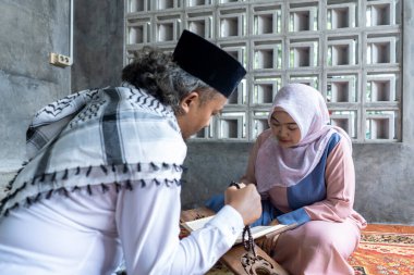 Kur 'an okumayı öğreniyorlardı. İki Endonezyalı kadın ve erkek evde Kur 'an okumayı öğreniyor. Kuran 'ı okuyorlar.