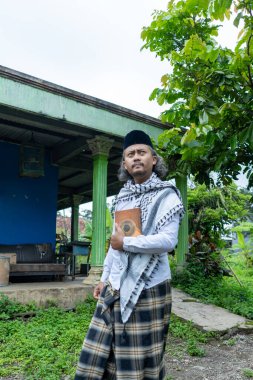 Al Quran taşıyan ve tipik Endonezya kıyafetleri giyen bir adam.