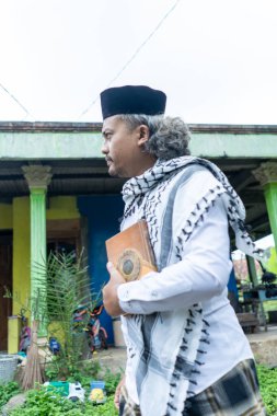 Al Quran taşıyan ve tipik Endonezya kıyafetleri giyen bir adam.