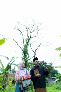 Bir çift genç Endonezyalı kadın ve erkek Müslüman kıyafetleri giyip Kuran 'a gidiyorlar. Kur 'an ve namaz araçlarını taşırlar..