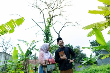 Bir çift genç Endonezyalı kadın ve erkek Müslüman kıyafetleri giyip Kuran 'a gidiyorlar. Kur 'an ve namaz araçlarını taşırlar..