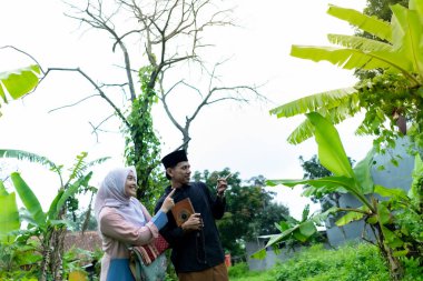 Bir çift genç Endonezyalı kadın ve erkek Müslüman kıyafetleri giyip Kuran 'a gidiyorlar. Kur 'an ve namaz araçlarını taşırlar..