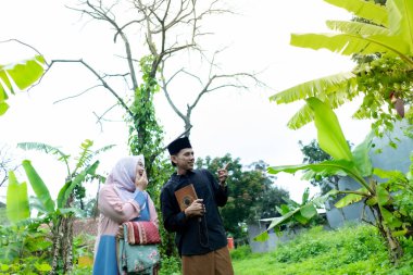 Bir çift genç Endonezyalı kadın ve erkek Müslüman kıyafetleri giyip Kuran 'a gidiyorlar. Kur 'an ve namaz araçlarını taşırlar..