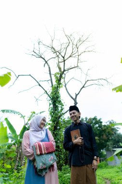 Bir çift genç Endonezyalı kadın ve erkek Müslüman kıyafetleri giyip Kuran 'a gidiyorlar. Kur 'an ve namaz araçlarını taşırlar..