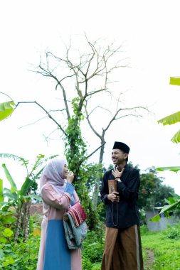 Bir çift genç Endonezyalı kadın ve erkek Müslüman kıyafetleri giyip Kuran 'a gidiyorlar. Kur 'an ve namaz araçlarını taşırlar..