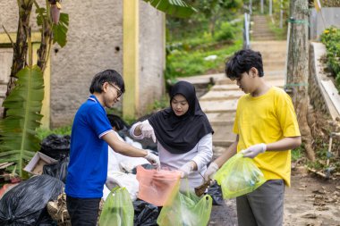 Çöp toplama. Bir grup Asyalı genç plastik atıkları ayırıyor. İnsanlar çöplerle uğraşırken görülüyor..