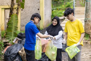Çöp toplama. Bir grup Asyalı genç plastik atıkları ayırıyor. İnsanlar çöplerle uğraşırken görülüyor..