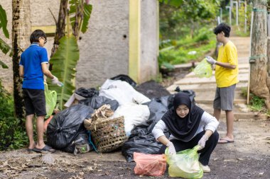 Çöp toplama. Bir grup Asyalı genç plastik atıkları ayırıyor. İnsanlar çöplerle uğraşırken görülüyor..