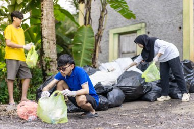 Çöp toplama. Bir grup Asyalı genç plastik atıkları ayırıyor. İnsanlar çöplerle uğraşırken görülüyor..