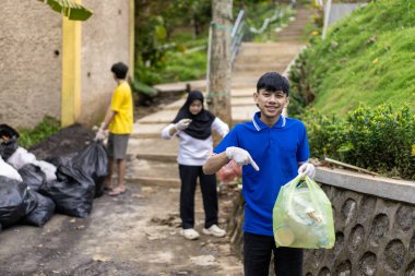 Çöp toplama. Bir grup Asyalı genç plastik atıkları ayırıyor. İnsanlar çöplerle uğraşırken görülüyor..