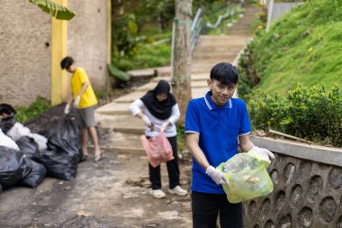 Çöp toplama. Bir grup Asyalı genç plastik atıkları ayırıyor. İnsanlar çöplerle uğraşırken görülüyor..