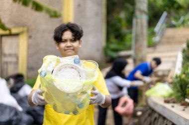 Çöp toplama. Bir grup Asyalı genç plastik atıkları ayırıyor. İnsanlar çöplerle uğraşırken görülüyor..