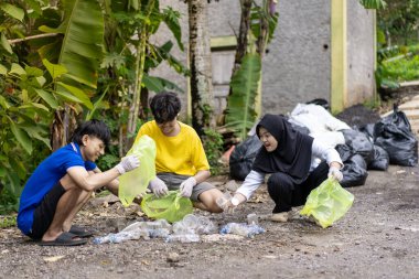 Çöp toplama. Bir grup Asyalı genç plastik atıkları ayırıyor. İnsanlar çöplerle uğraşırken görülüyor..