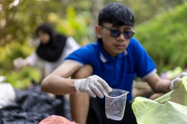 Çöp toplama. Bir grup Asyalı genç plastik atıkları ayırıyor. İnsanlar çöplerle uğraşırken görülüyor..