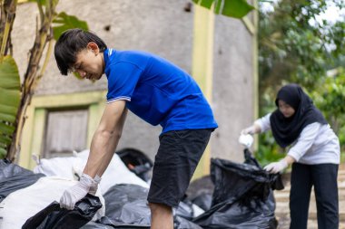 Çöp toplama. Bir grup Asyalı genç plastik atıkları ayırıyor. İnsanlar çöplerle uğraşırken görülüyor..