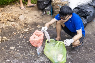 Çöp toplama. Bir grup Asyalı genç plastik atıkları ayırıyor. Bir adam çöp toplarken görülüyor..