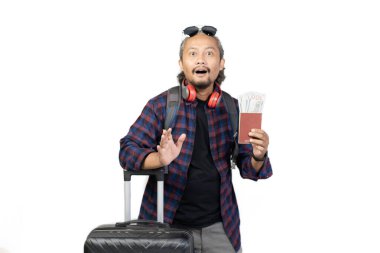 Kıvırcık saçlı Endonezyalı adam seyahat ederken para dolu valiz ve pasaport taşıyor, seyahat konsepti, beyaz arka planda izole edilmiş..