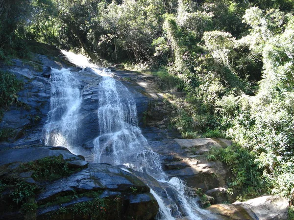 Tijuca Ormanı 'ndaki şelale, Rio de Janeiro, kayalık çıkıntılar, benekli yan aydınlatma ve sürekli bir su akışı. Güneş ışınları görüntünün sağ köşesini nazikçe öperek bu doğal mucizeye biraz sihir katar..