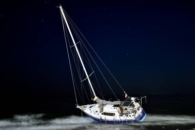 Sailboat aground and sunken on the beach at sunset clipart