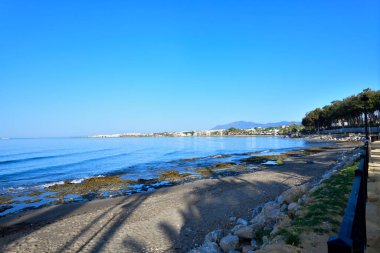 Sahilde kayalıklar ve ön planda tırabzanlar var.