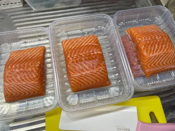 Mutfakta somon dilimlerini seramik bıçak ve sarı kesim tahtasıyla kesmek için taze somon hazırlığı.