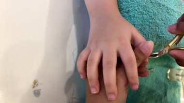 Asyalı küçük kızın elleri, yaz tatilinde sabah salonda manikür masasının üzerinde yetişkin personelin elleriyle manikür yaptırıyor.