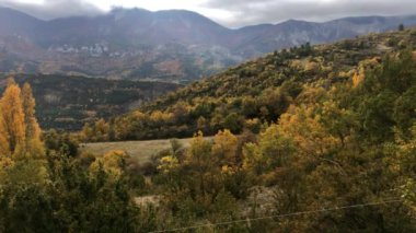 Une vallee dans les alpes francases on automne, la vallee du Jabron, avec des arbres aux feuilles jaunes et portakal, l 'herbe encore verte et un ciel nuageux.