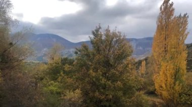 Une vallee dans les alpes francases on automne, la vallee du Jabron, avec des arbres aux feuilles jaunes et portakal, l 'herbe encore verte et un ciel nuageux.