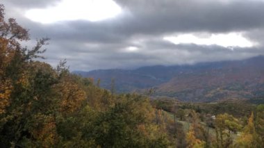 Une vallee dans les alpes francases on automne, la vallee du Jabron, avec des arbres aux feuilles jaunes et portakal, l 'herbe encore verte et un ciel nuageux.