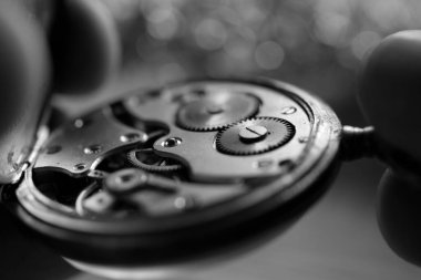 Saatin kadranını inceleyen bir saatçinin siyah beyaz yakın plan fotoğrafı.