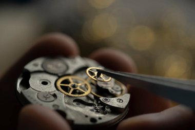 Mans eller eski saati onarıyor, cımbızla bir parça tutuyor.