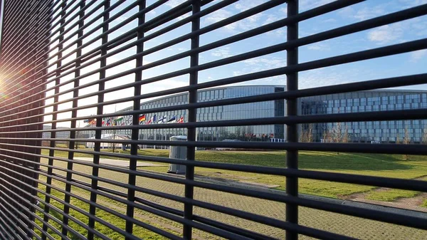 Finlandiya 'nın NATO' ya katılım tarihi olan 4 Nisan 2023 tarihinde, NATO Genel Merkezi 'nde (Brüksel) Finlandiya bayrağı dalgalanmaktadır. Çitin arkasından çekilmiş, çitin üzerinde güneş ışınları var..