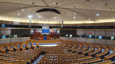 Empty, half-lit plenary chamber (hemicycle) of the European Parliament in Brussels. View from the visitors' gallery, with the ceiling visible. December 2023. clipart