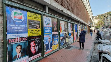 Sanremo 'da (İtalya) posterler duvarı. Siyasi reklamlar ve sinema reklamları. Posterlere bakan kadın.