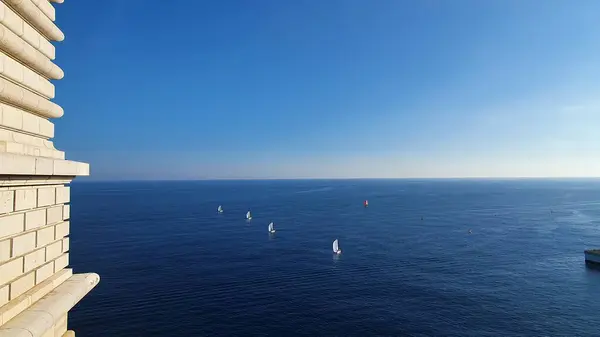 Monako, Ekim 2022. Akdeniz 'de beyaz yelkenliler sıra oluşturuyorlar. Derin mavi sulara karşı beyaz tuğlalı bir duvarın aksine.