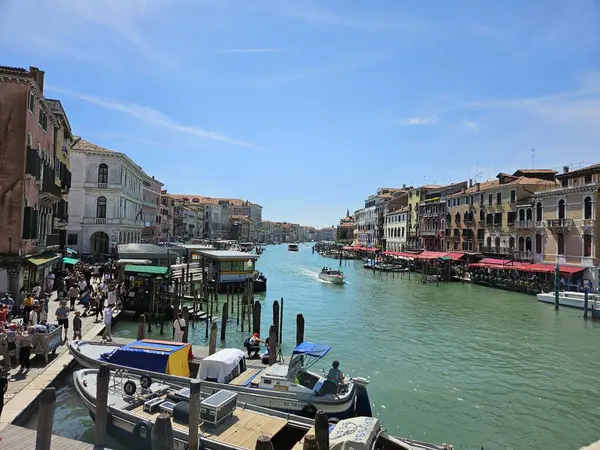 İtalya Venedik Büyük Kanalı (Mayıs 2024). Turkuaz suda süzülen sürat tekneleri, turistlerle dolu kaldırımlar. Aydınlık bir yaz gününde mavi gökyüzü.