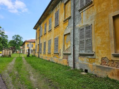 Monza, İtalya (Mayıs 2024). Çökmüş bir taş ve tuğladan yapılmış, pencereleri kapalı parlak sarı bir duvar. Monza Park 'ta terk edilmiş bir evin ön cephesi.).