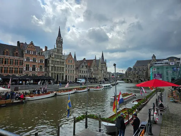 Gent, Belçika (Mayıs 2024): Şehir merkezindeki Leie Nehri üzerindeki kanal. Nehir tekneleri eski Flaman evlerinin önünde dizildi. Bulutlu bir günde, suyun yanında dalgalanan ülkelerin bayrakları.