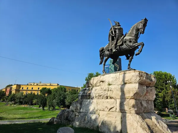 Tiran, Arnavutluk (Temmuz 2024). Başkentin ana meydanındaki Skanderbeg Anıtı, Arnavutluk 'un ulusal kahramanının anısına dikildi. Taş bir kaide üzerinde duran bir savaşçının at heykeli. Park ve binaların cepheleri uzaktan görülebiliyor..