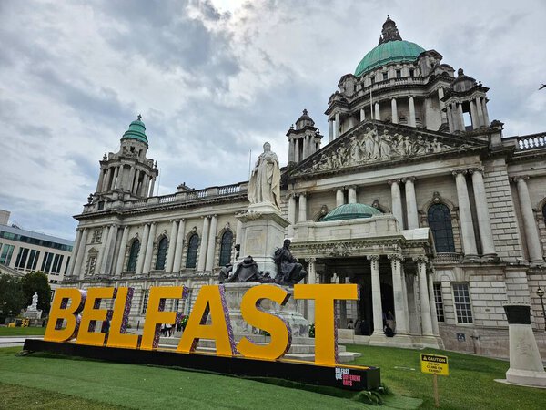 Belfast City Hall, July 2024. Yellow letters spelling out "Belfast", in front of an imposing baroque-style building. Statue of Queen Victoria standing in the foreground.