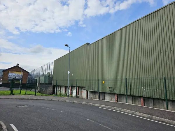 Belfast, Temmuz 2024: 'Barış Duvarı' (Barış Cephesi) Bombay Caddesi 'nde, Katolik ve Protestan mahallelerini ayırıyor. Kuzey İrlanda 'daki sorunlar yüzünden dikilmiş yeşil çit ve metal duvar. Uzaktan görünen bir duvar resmiyle sessiz, boş bir cadde..