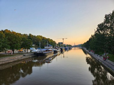 Turku, Finland (August 2024). Sunset over the Aura River on a quiet evening in the city centre. Restaurant boats docked at the riverbank. clipart