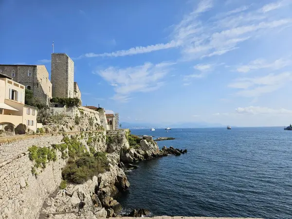 Antibes, Fransa (Ağustos 2024): Promenade Amiral-de-Grasse 'de sahil bulvarı. Akdeniz 'e bakan taş duvarlar, kayalar ve kuleler aydınlık bir yaz gününde.