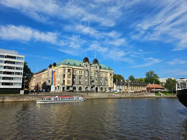 Turku City ofis binası Aura Nehri 'nin karşısından izleniyor. Ağustos 2024 'te Finlandiya' da yaz öğleden sonra. Art Nouveau binasının önünde Ukrayna ve Gurur bayrakları sergilendi.