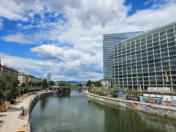 Viyana, Avusturya (Mayıs 2025): Tuna Nehri 'nin görüntüsü kent merkezindeki Donaukanal üzerinden aktarıldı. Grafiti ve kule blokları pofuduk beyaz bulutların altında.