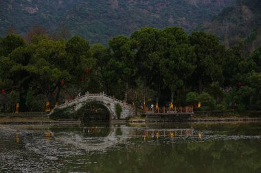 Geleneksel bir Çin bahçesinde sakin bir göletin üzerinde eğri bir taş köprü..