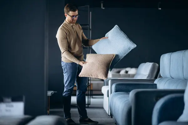 Young man buying pillows and sofa in furniture store