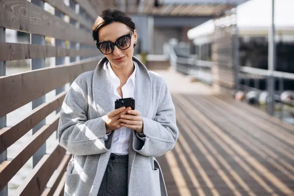 ストリートを歩いて携帯電話を使用して灰色のコートの女性の肖像 — ストック写真
