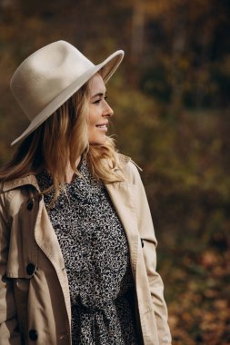 Güz parkında yürürken şapka ve palto giyen güzel bir kadın.